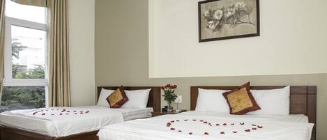 A hotel room with two beds, each with white linens and decorative pillows. A painting of flowers hangs on the wall above the beds.