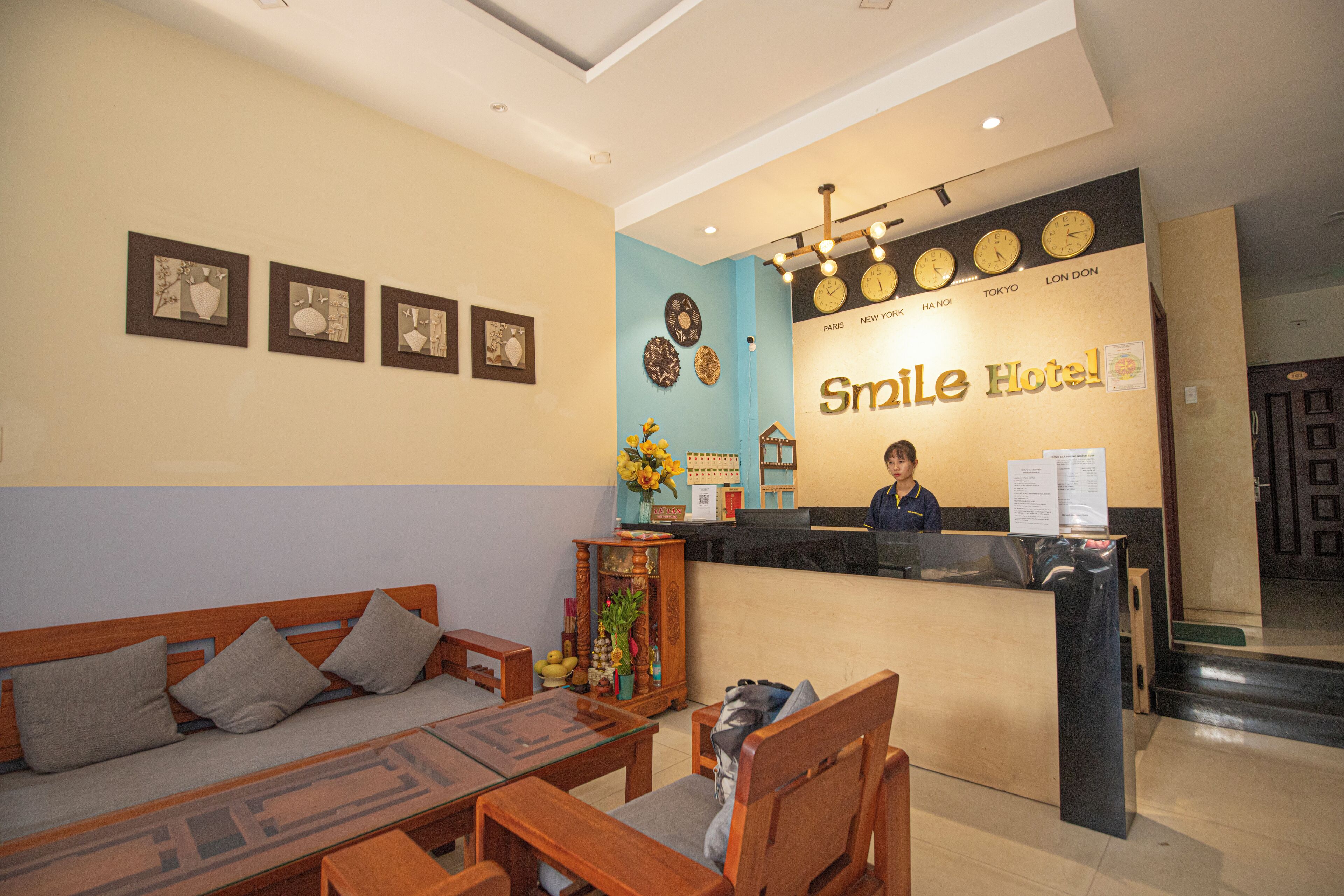 A reception desk with a sign for Smile Hotel, a receptionist, and a seating area with a sofa and chairs.