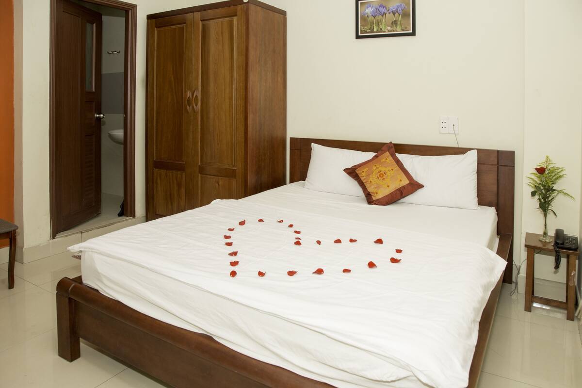 A neatly made bed with a heart-shaped arrangement of rose petals on the bedspread.