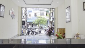 Un área de recepción con un puerta de vidrio que da a la calle, un mostrador de recepción y una planta.