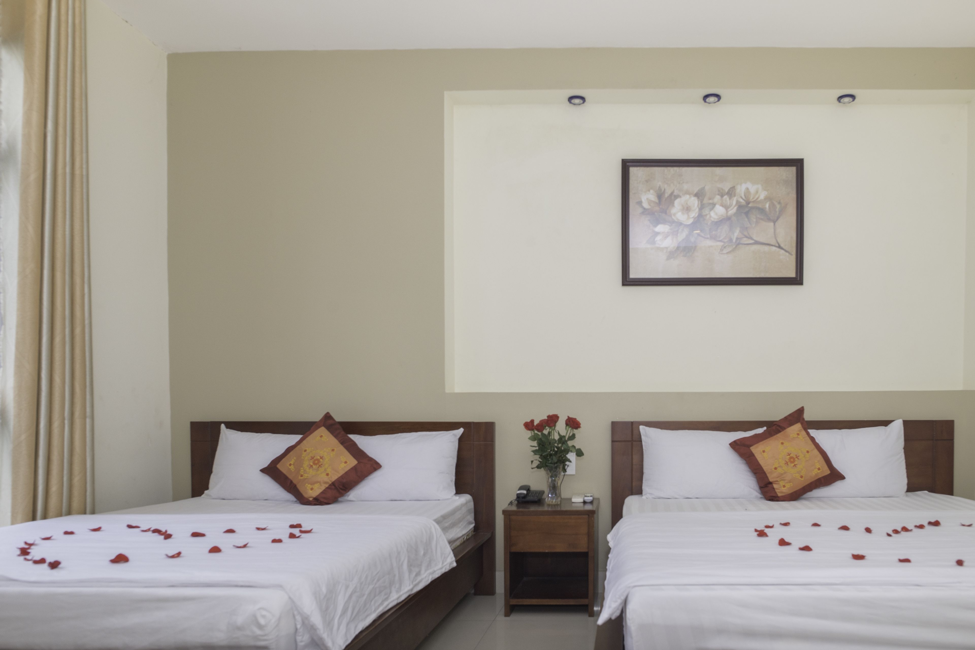 A hotel room with two beds, a nightstand with a vase of flowers, and a framed picture on the wall.