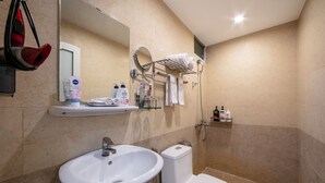 A bathroom with a sink, toilet, and shower. There are toiletries on the wall and a towel rack. - A25 Hotel - 109 Truc Bach (Hanoi)