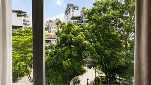 A view through a window of a building with a street and trees in the foreground, and other buildings in the background. - A25 Hotel - 109 Truc Bach (Hanoi)
