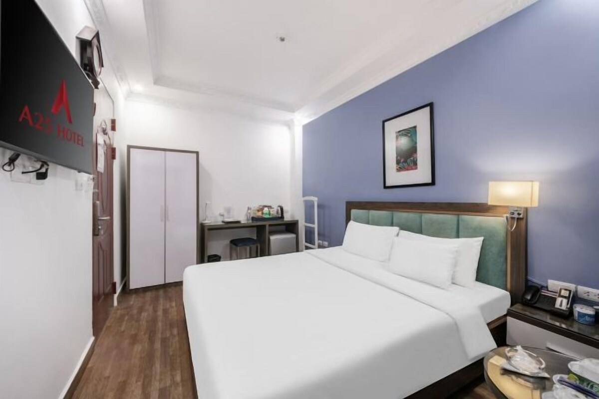 A hotel room with a large bed, a desk with a chair, a nightstand, and a wall-mounted telephone.