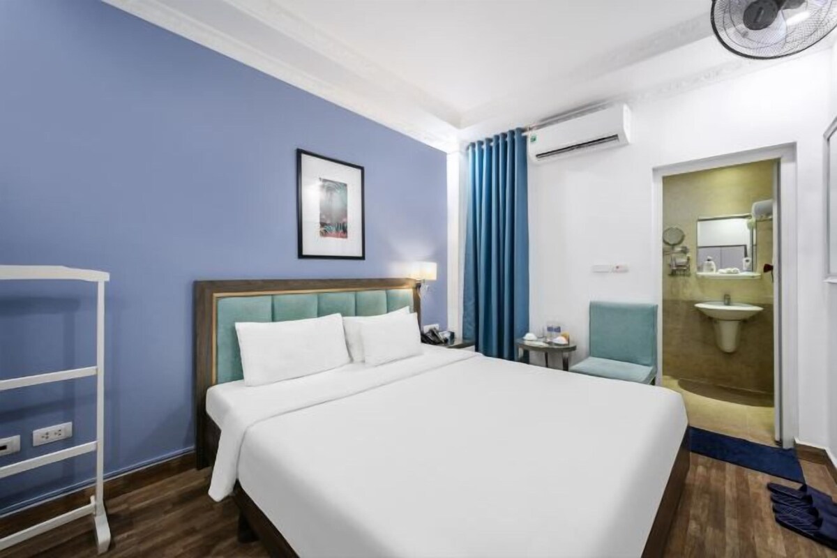 Une chambre d’hôtel avec un lit, une chaise, une petite table, un lavabo et un miroir.