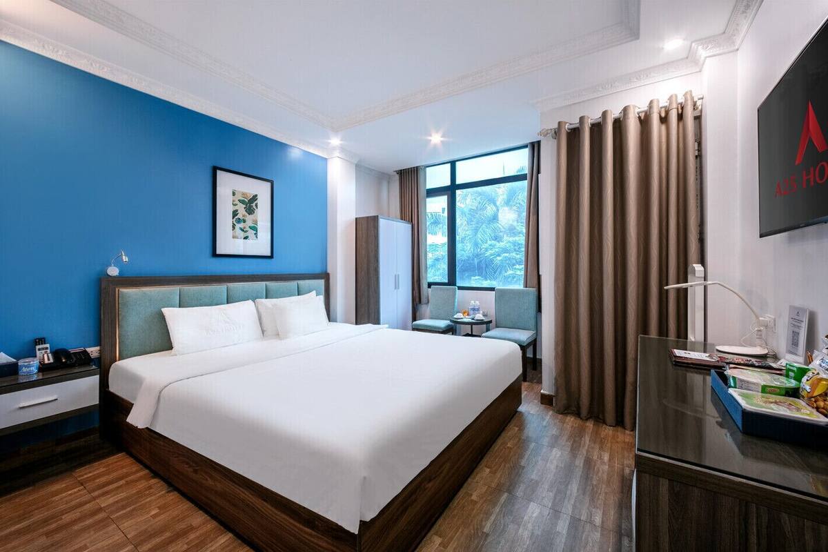 Una habitación de hotel con una cama grande, un escritorio con lámpara, una silla, una ventana con cortinas y un televisor en la pared.