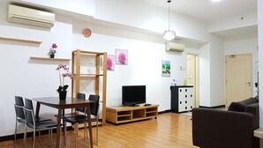 A modern living room with a wooden dining table, chairs, a sofa, and a TV. There are air conditioning units, a clock, and artwork on the walls. - Citylise Studio (Kuala Lumpur)