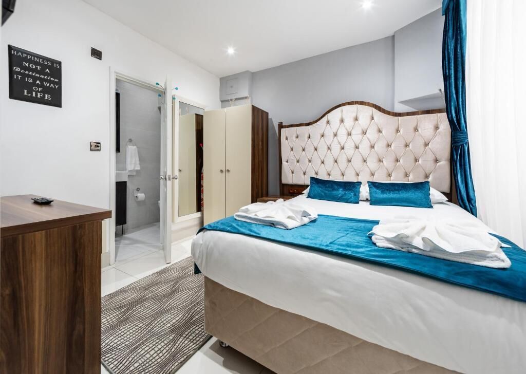 A hotel room with a bed, a desk, a wardrobe, and a bathroom visible through an open door.