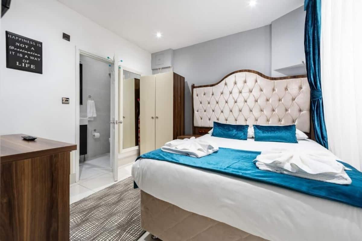 A hotel room with a bed, a desk, a wardrobe, and a bathroom visible through an open door.