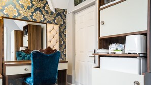 A compact room with a vanity, a blue chair, a white cabinet, and a mirror. - Vilenza Hotel (London)