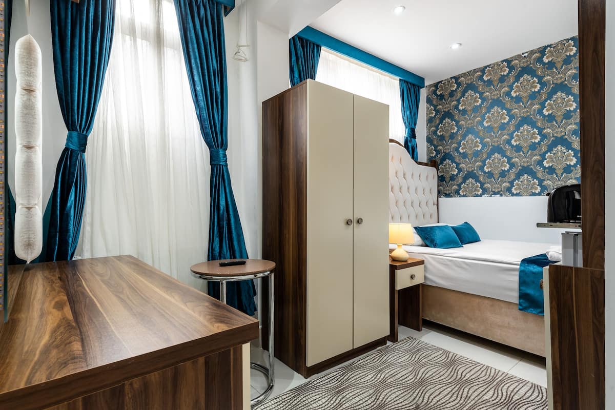 A modern bedroom with a wooden desk, a wardrobe, a bed with blue bedding, and a patterned wall.