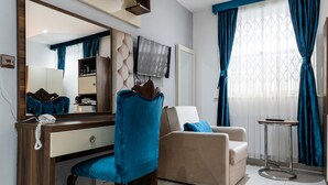 A modern hotel room with a large mirror, a desk with a telephone, a sofa, and a TV. - Vilenza Hotel (London)