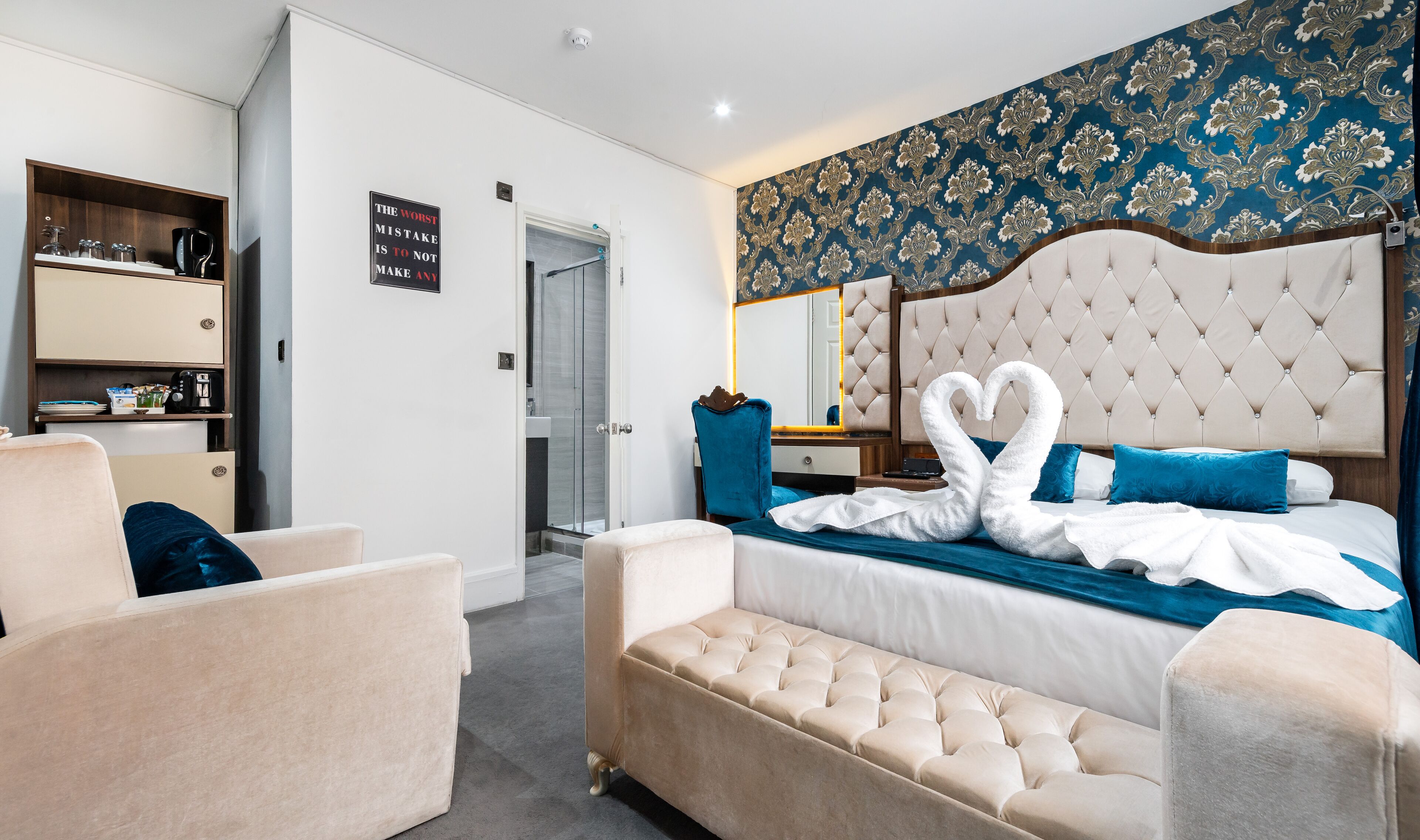 A hotel room with a large bed, a sitting area, a vanity, and a wardrobe.