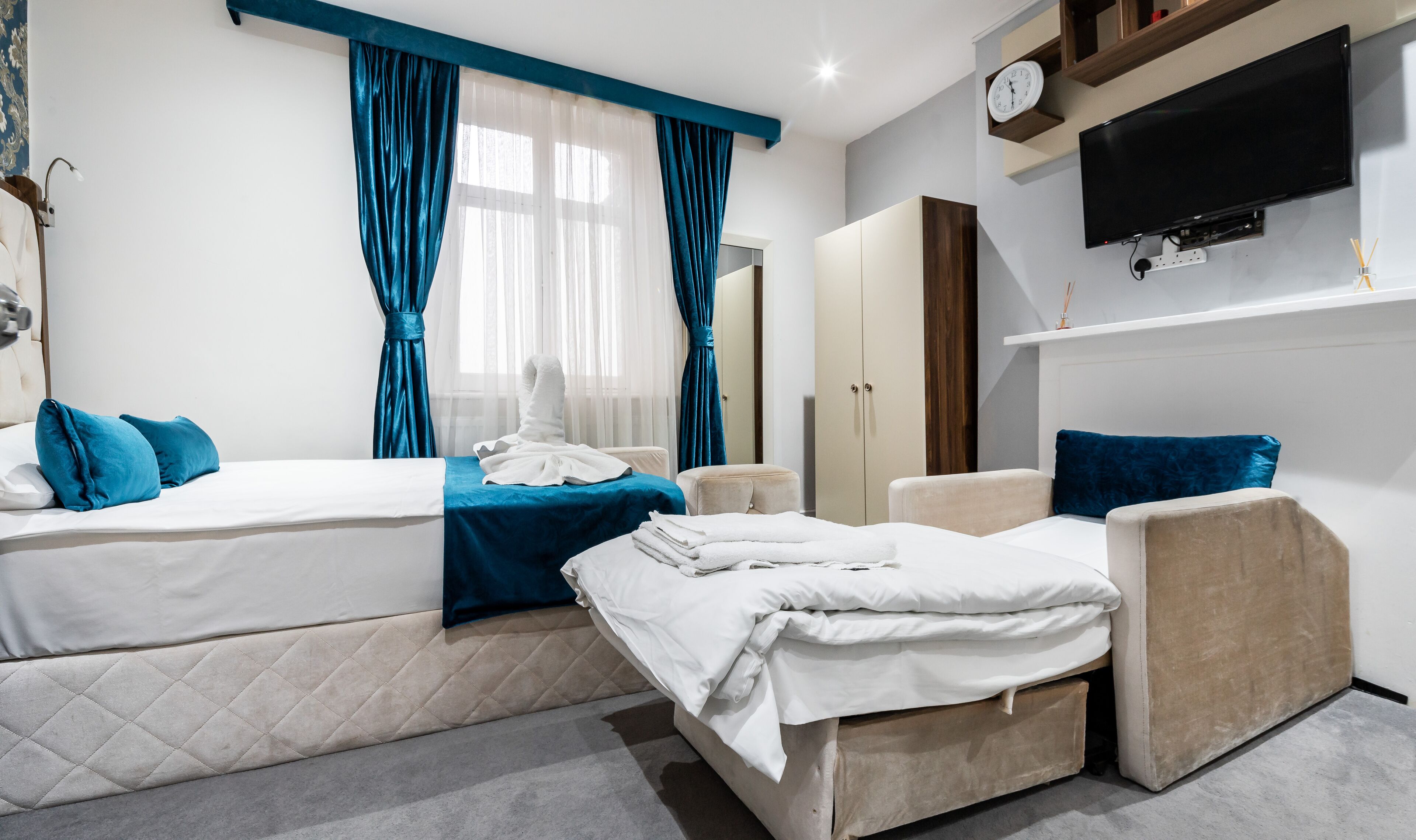 A hotel room with two beds, a TV, a clock, and a wardrobe.