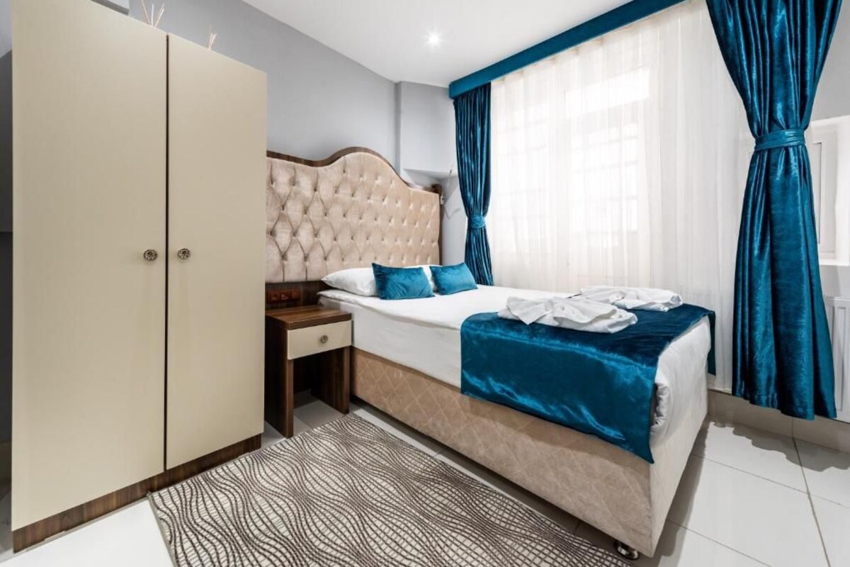 A bedroom with a bed, a wardrobe, a nightstand, and a window with curtains.