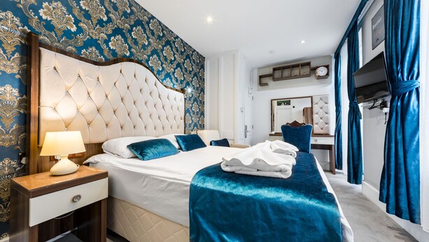 A hotel room with a large bed, a nightstand, a lamp, a TV, and a mirror. - Vilenza Hotel (London)