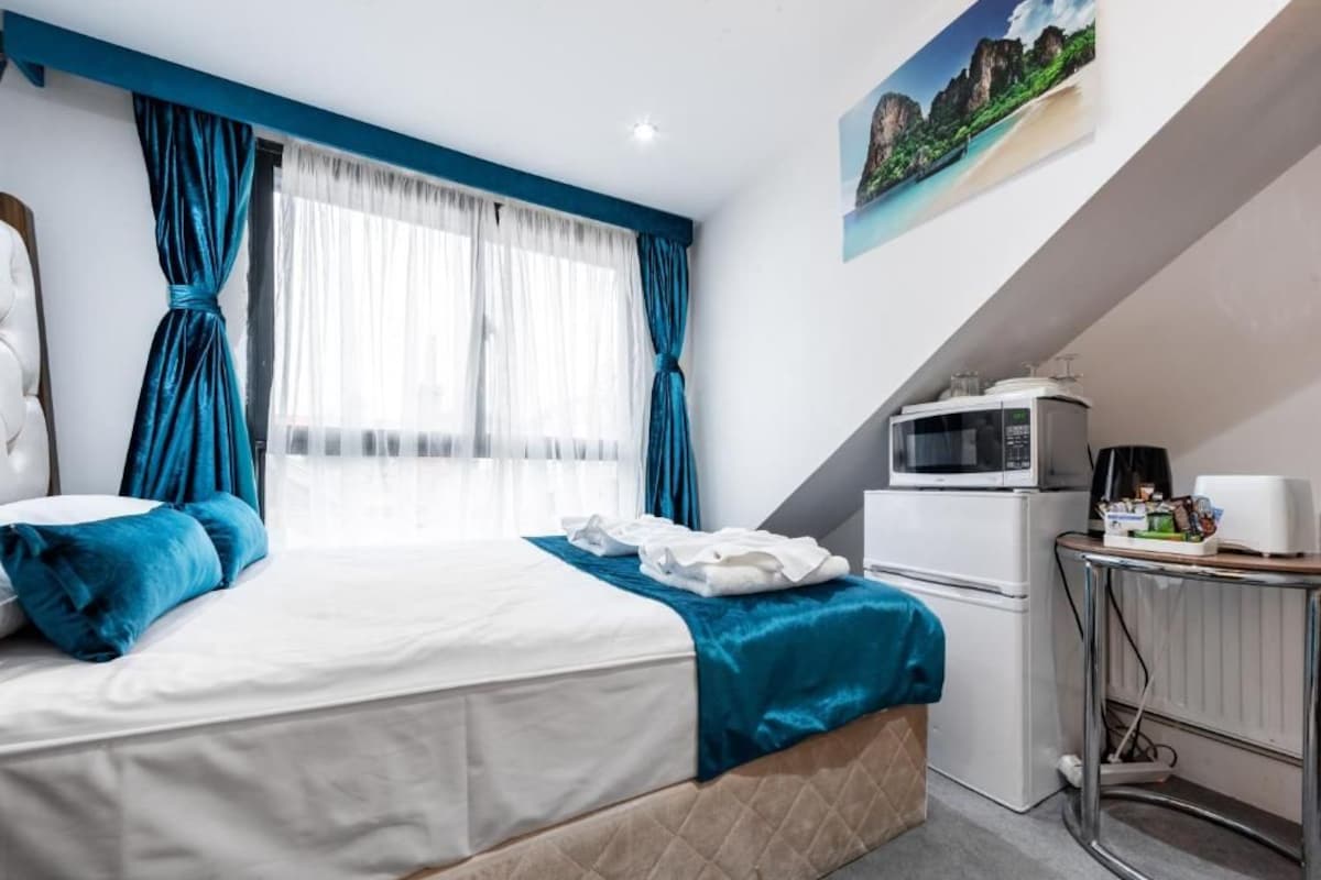 A bedroom with a bed, a desk, a microwave, and a painting on the wall.
