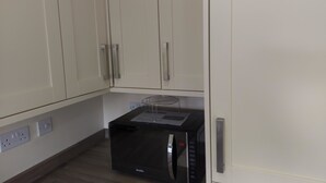 A kitchenette with a black microwave, a small wire rack, and a power outlet. - Jaylets Budget Glenfield (Leicester)