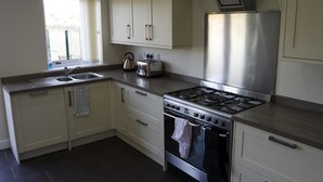 A modern kitchen with a stainless steel stove, oven, and sink. There are cabinets and a window with a view outside. - Jaylets Budget Glenfield (Leicester)
