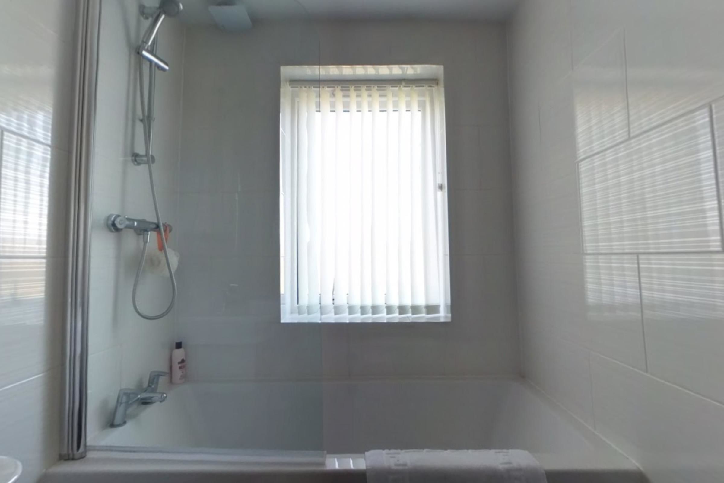 Ein kleiner, abgeschlossener Duschbereich mit Fenster, einer Handbrause und einem am Wand montierten Wasserhahn.