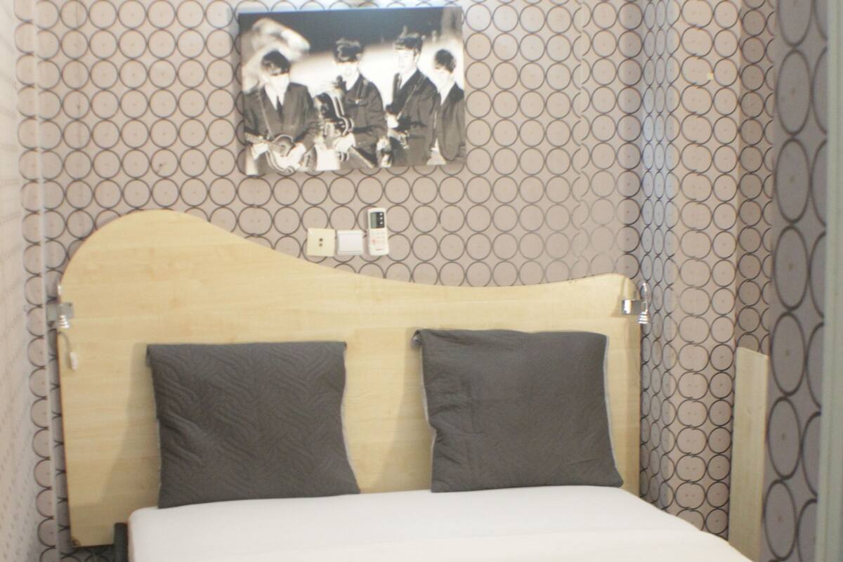 A bedroom with a bed, headboard, pillows, and a wall-mounted shelf with a photo.