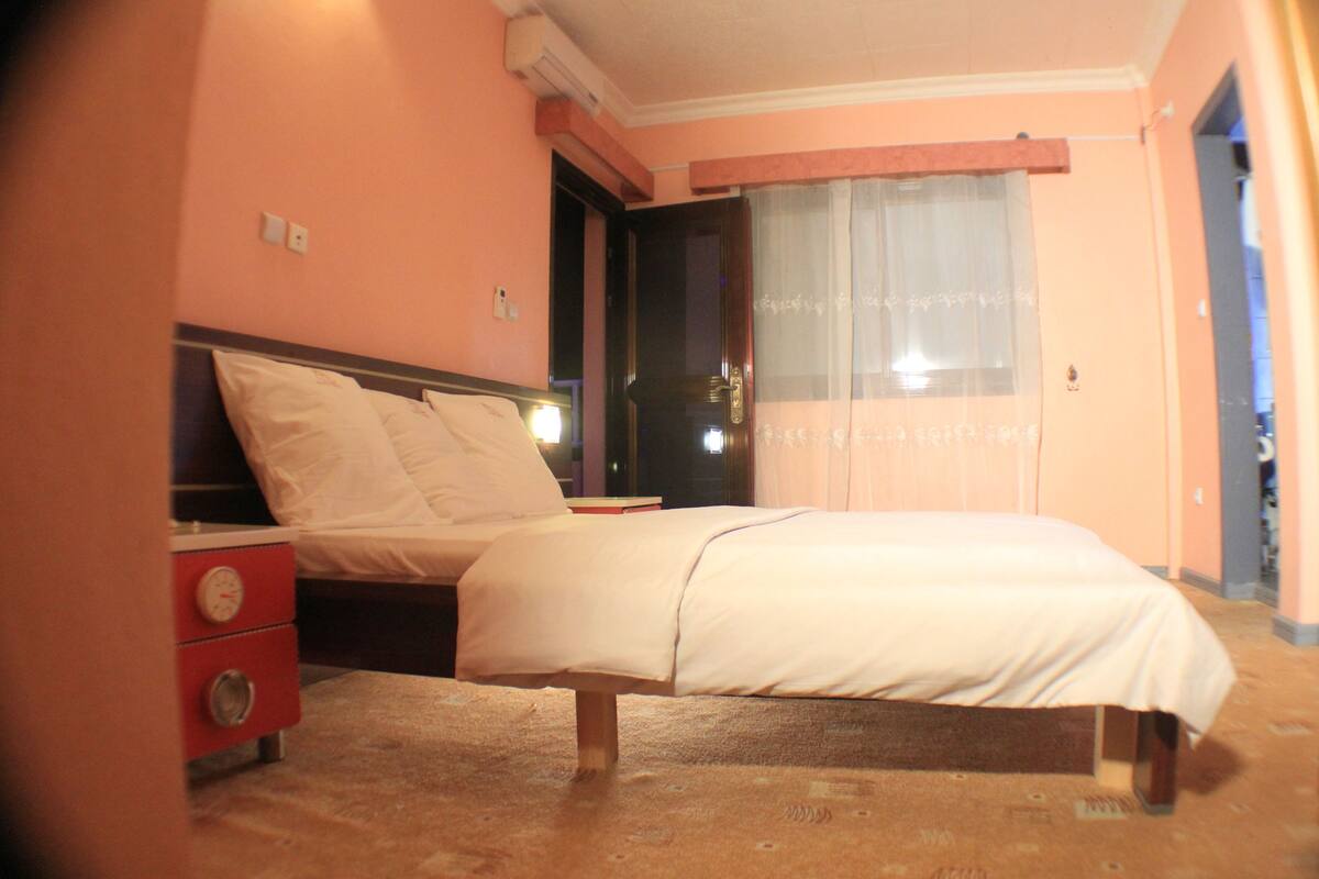 A bedroom with a bed, a nightstand, and a window with curtains.
