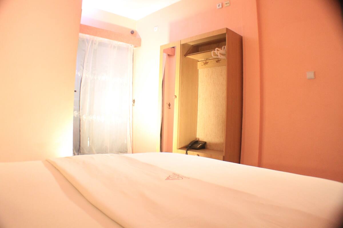 A hotel room with a bed, a wooden wardrobe, and a mirror.