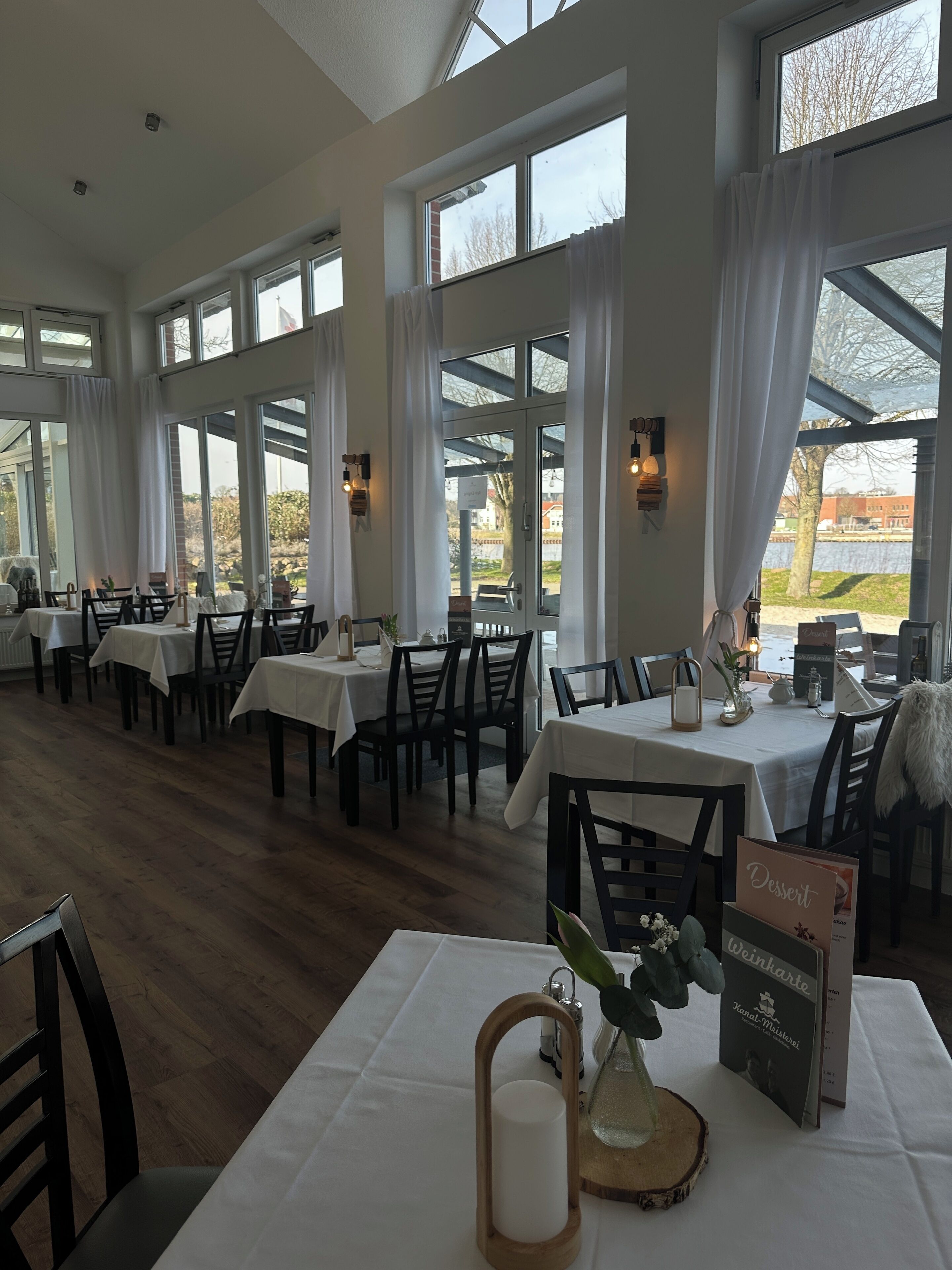Un restaurant doté de nombreuses tables et chaises, de grandes fenêtres et offrant une vue sur l’extérieur.