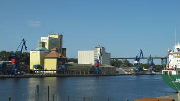 A waterfront industrial area with cranes, a large green ship, and buildings with signage.