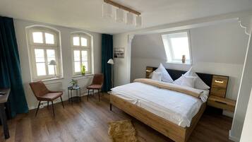 Een hotelkamer met een groot bed, een bureau met stoel, een kleine tafel en een raam met gordijnen.