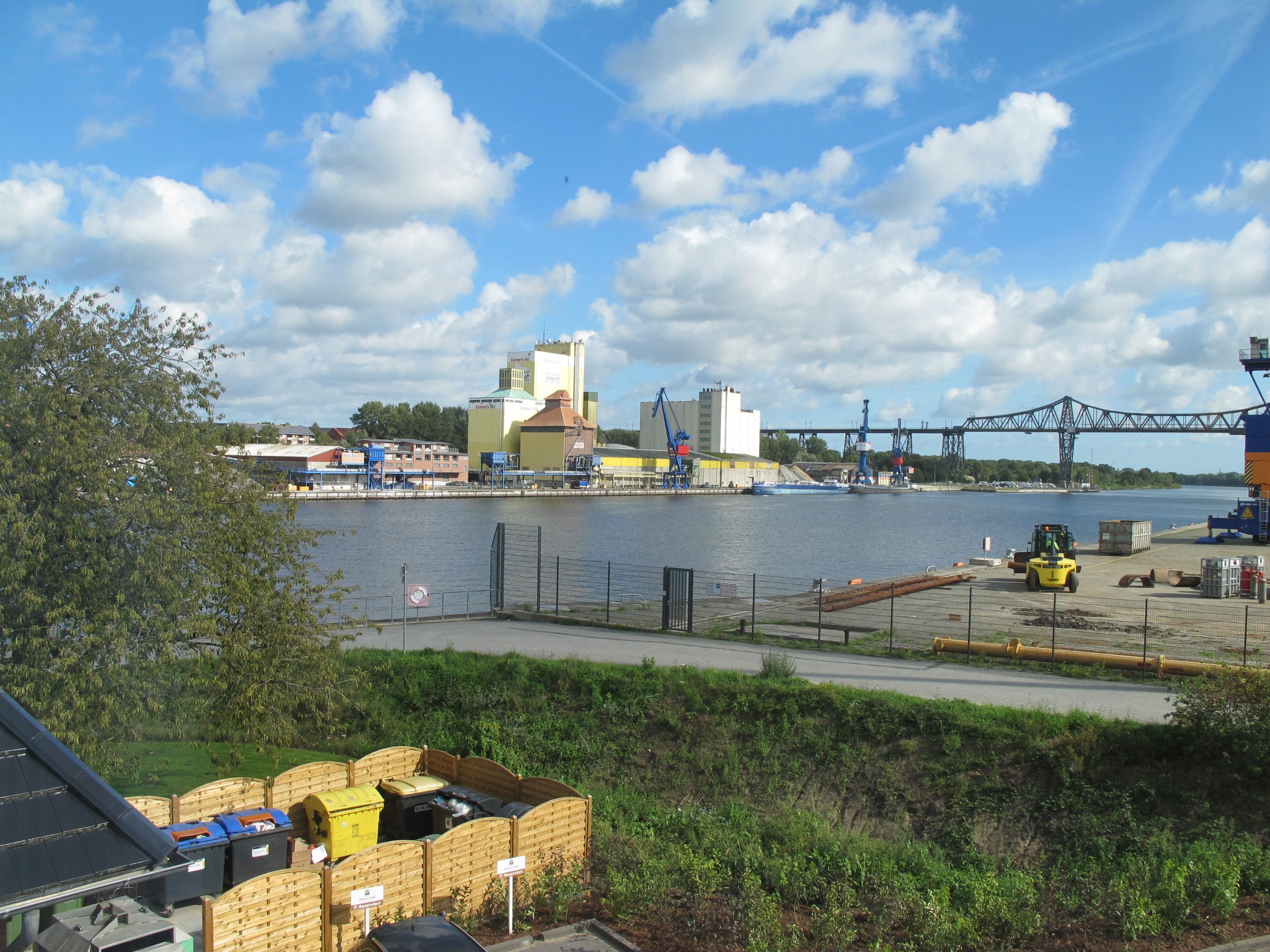 A waterfront industrial area with a bridge, a forklift, and shipping containers.