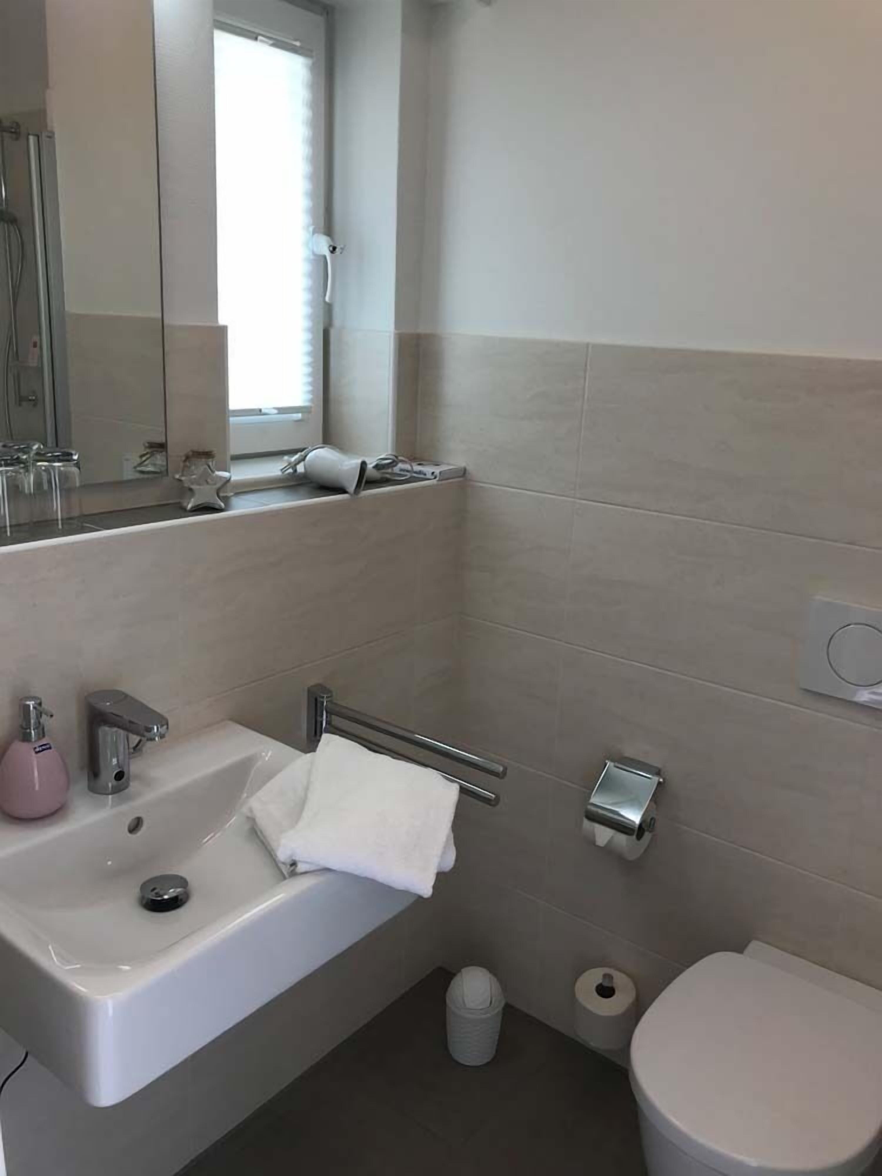 Un bagno moderno con lavandino, specchio, porta asciugamani, water e cestino.