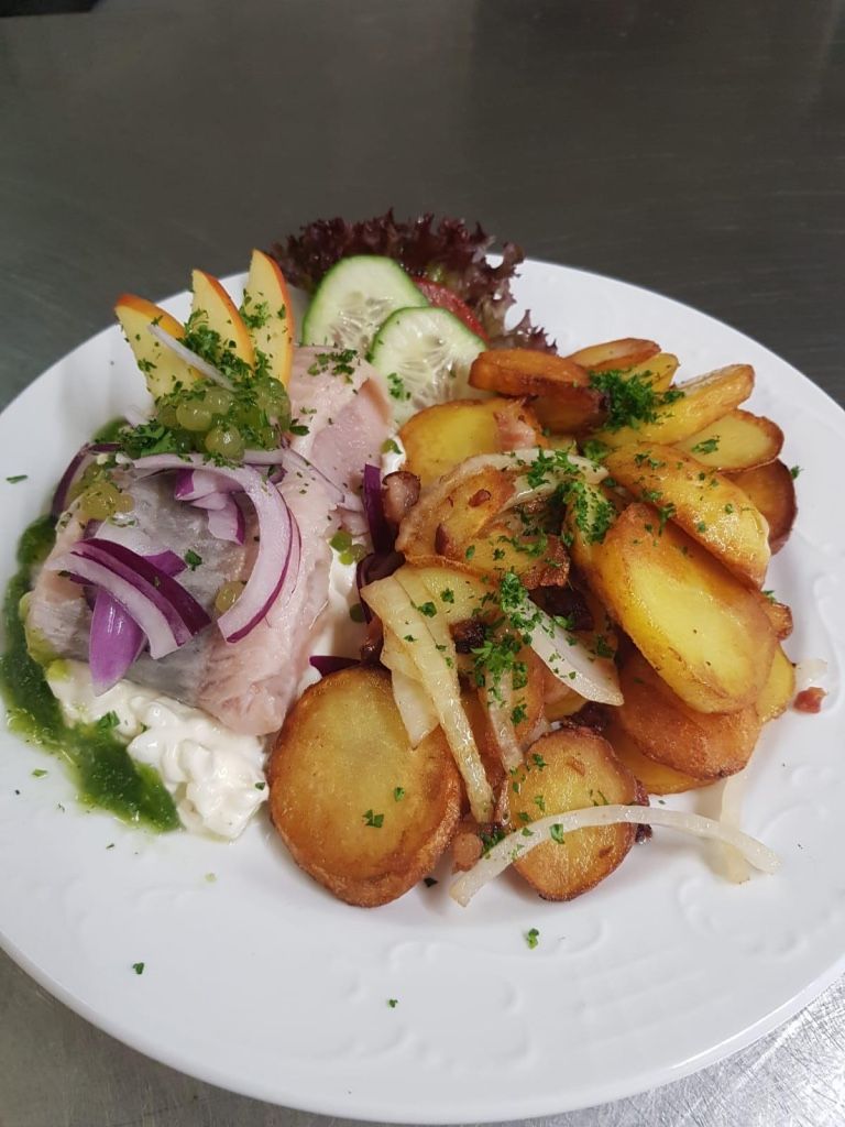 A plate of food with potatoes, onions, and a slice of meat, garnished with herbs.