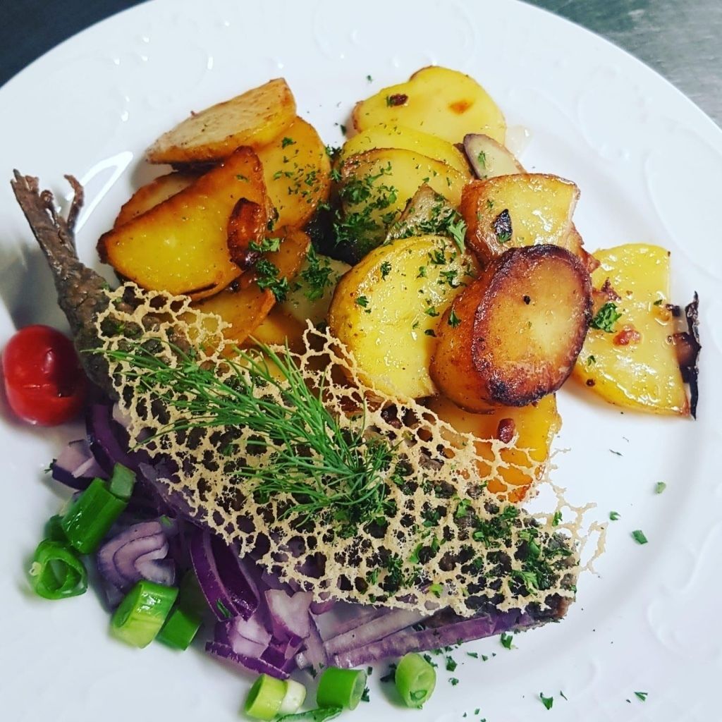 A plate of roasted potatoes garnished with herbs and a decorative net.