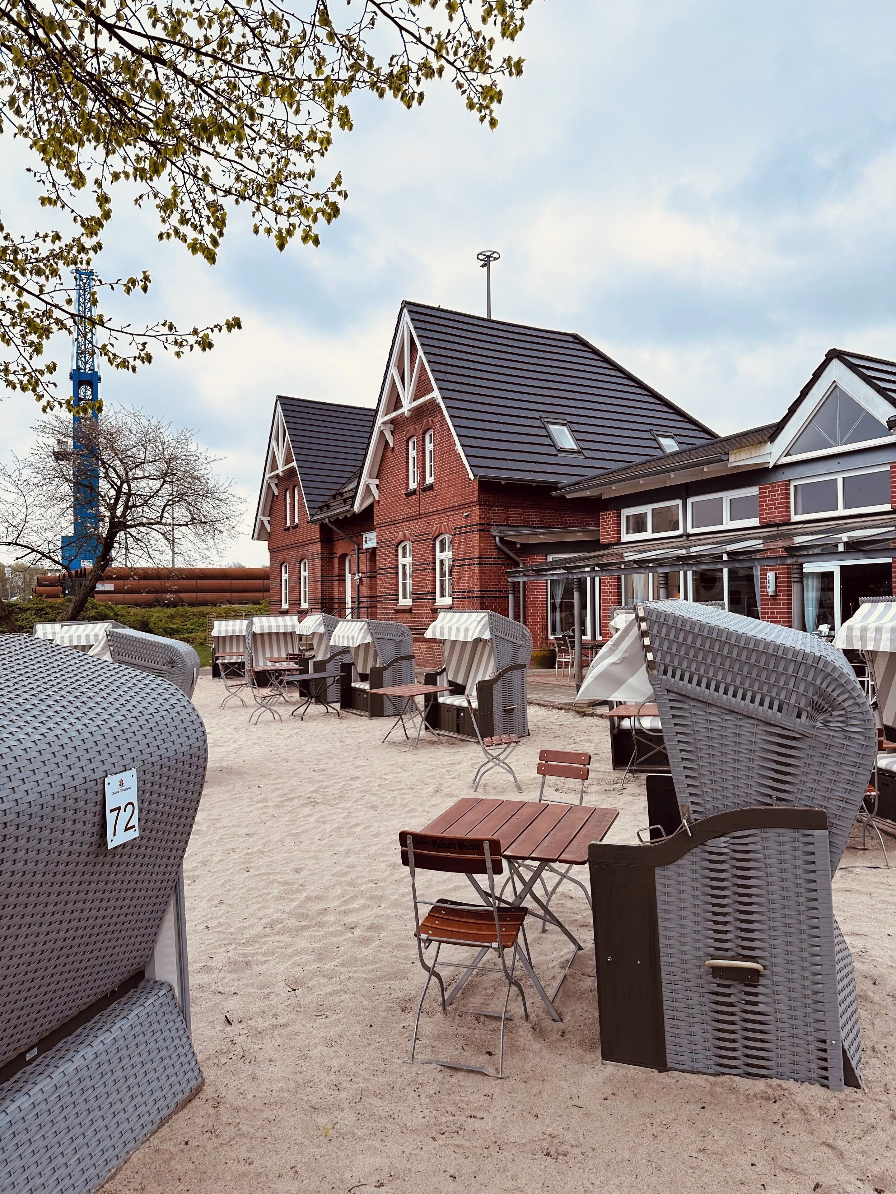 A beachside outdoor seating area with wicker furniture and a red brick building in the background.