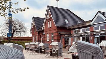A beachside outdoor seating area with wicker furniture and a red brick building in the background.