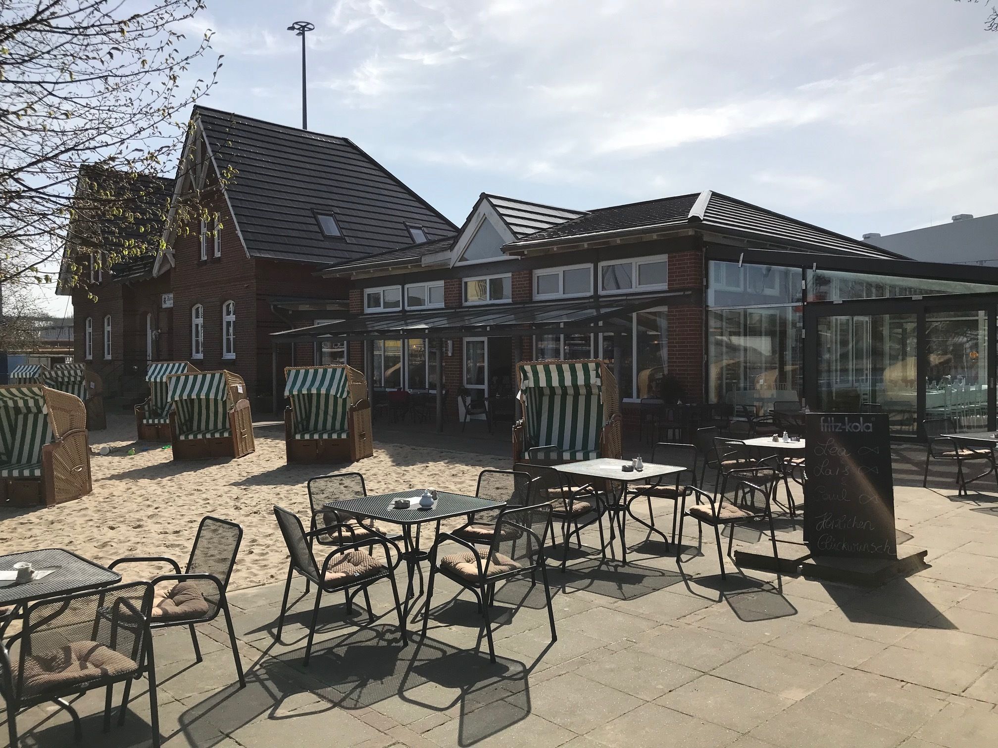 An outdoor seating area with wicker chairs and tables, a brick building with large windows, and a glass enclosure.
