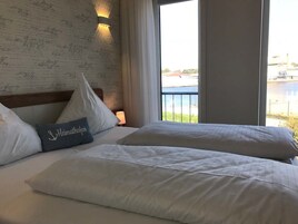 Ein Hotelzimmer mit zwei Betten, einem großen Fenster mit Blick auf ein Gewässer und Gebäude sowie einer Wand mit Unterschriften.