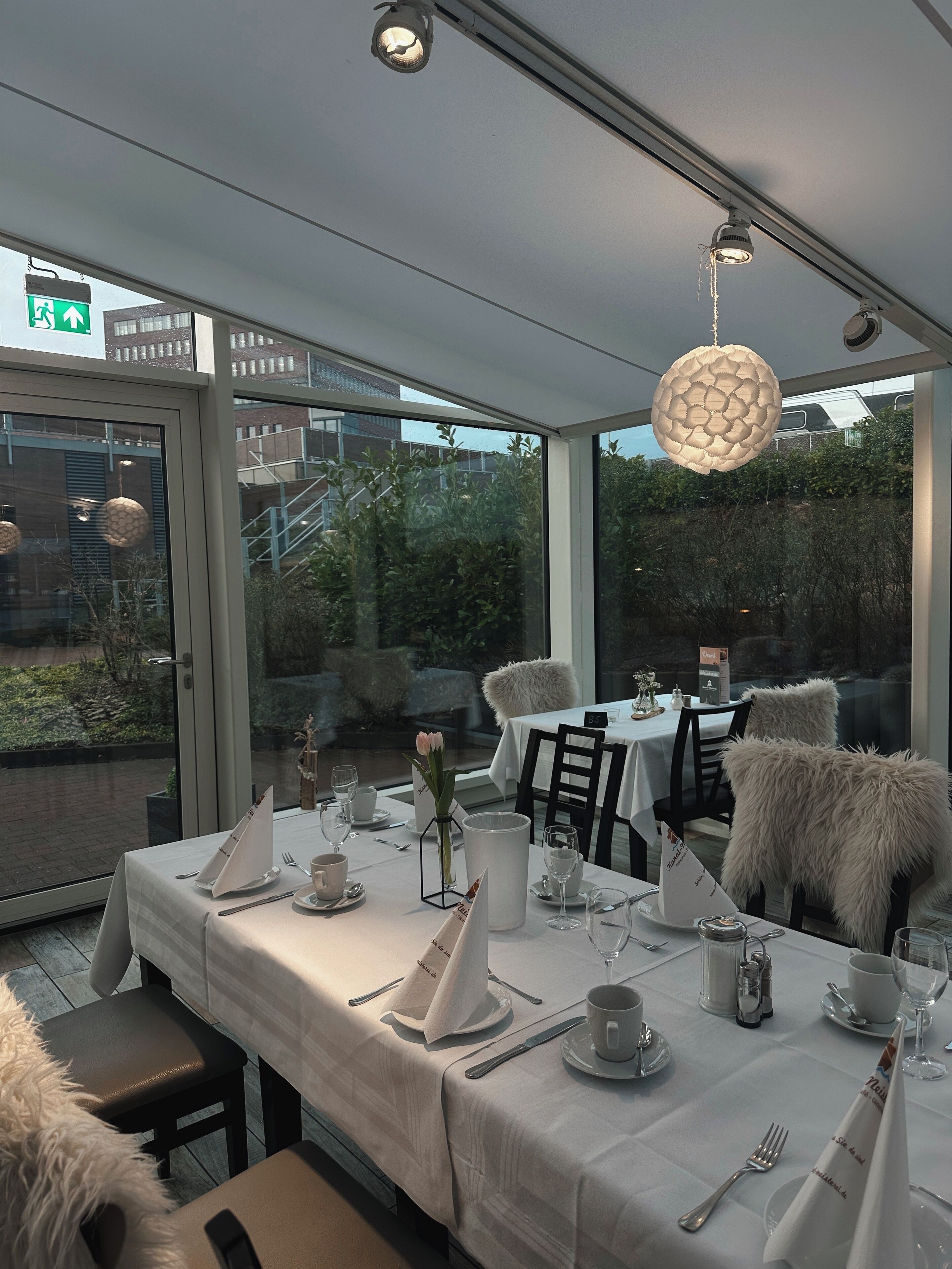A restaurant with tables set for dining, a hanging light fixture, and a view of the outside.