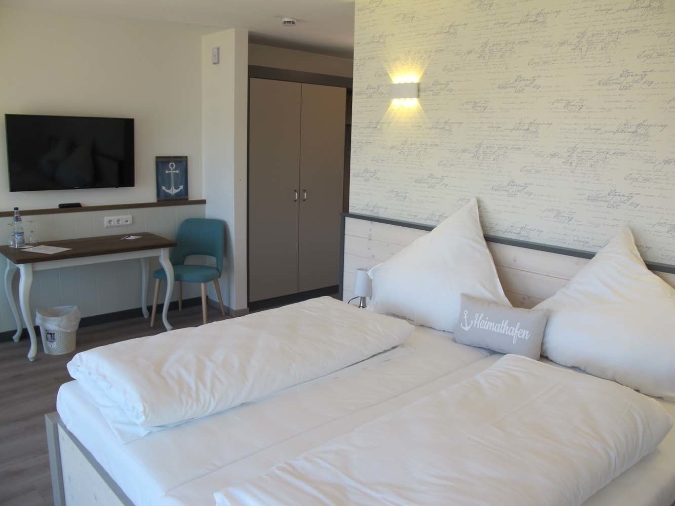 A hotel room with a bed, a desk, a chair, a television, and a wardrobe.
