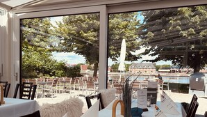An outdoor dining area with white tablecloths, wooden chairs, and a view of a lake and trees. - Kanal-Haus "Das Gästehaus direkt am Nord-Ostsee-Kanal" (Osterrönfeld)