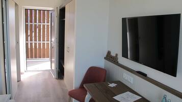 Habitación de hotel con un escritorio de madera, una silla roja, un televisor de pantalla plana y un ventanal corredero que da a un balcón.