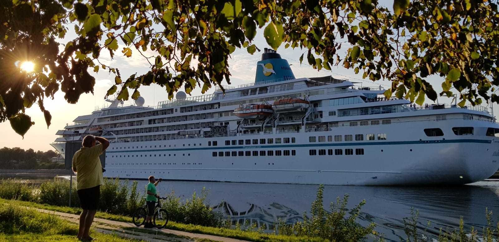 Een groot cruiseschip in de haven, met iemand die een foto maakt en een andere fietser in de buurt.