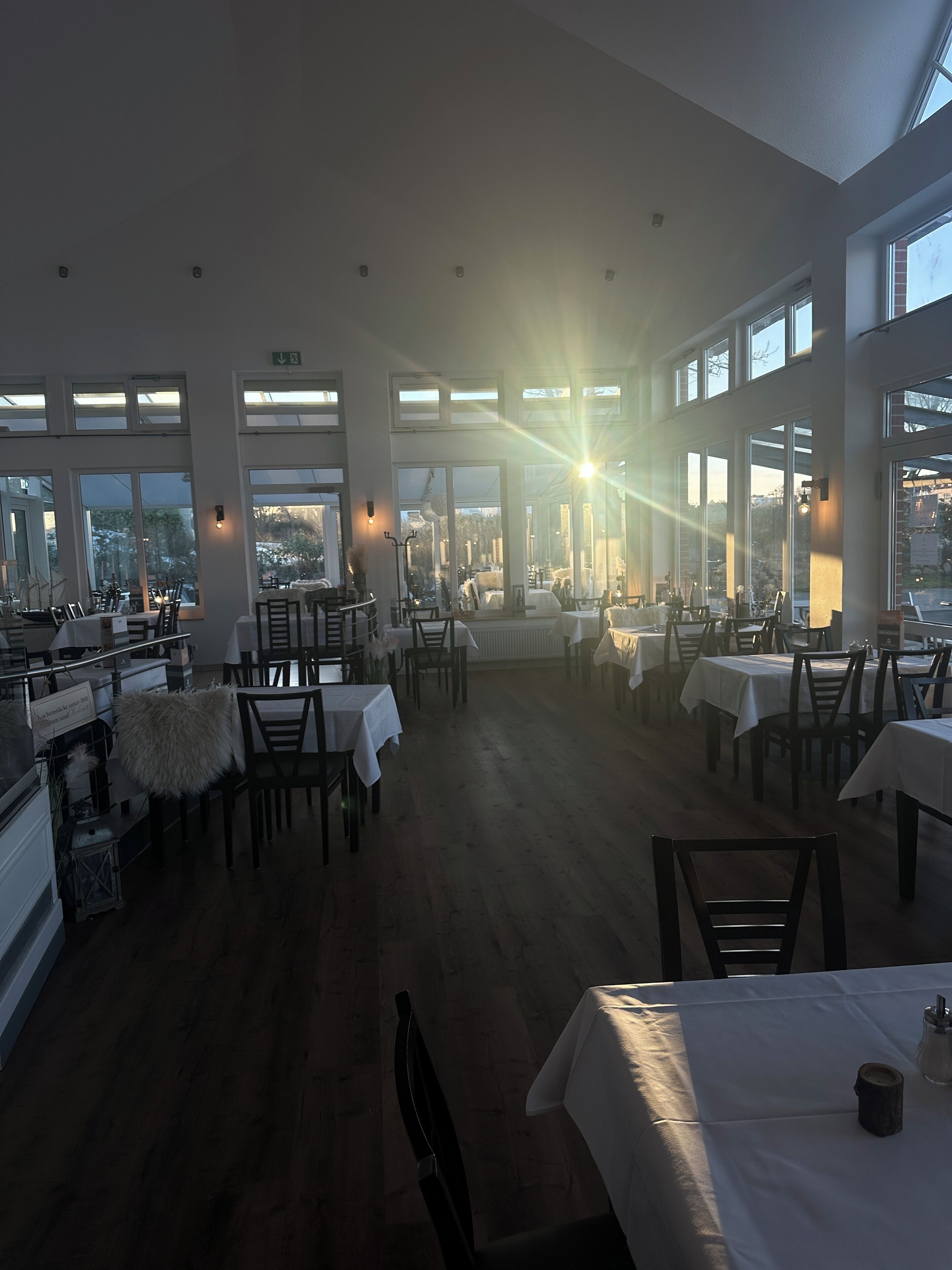 A spacious restaurant with high ceilings and large windows, offering views of the cityscape. Tables are neatly arranged, and the interior features modern lighting fixtures.