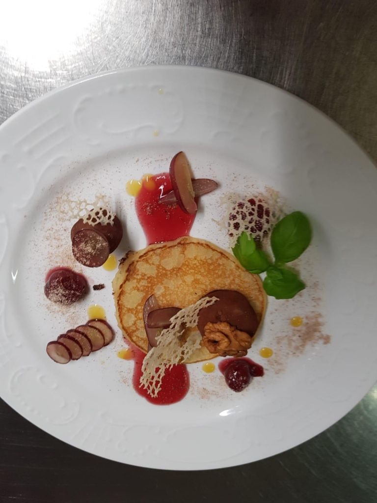 Ein weißer Teller mit Pfannkuchen, Schokolade und Beeren.