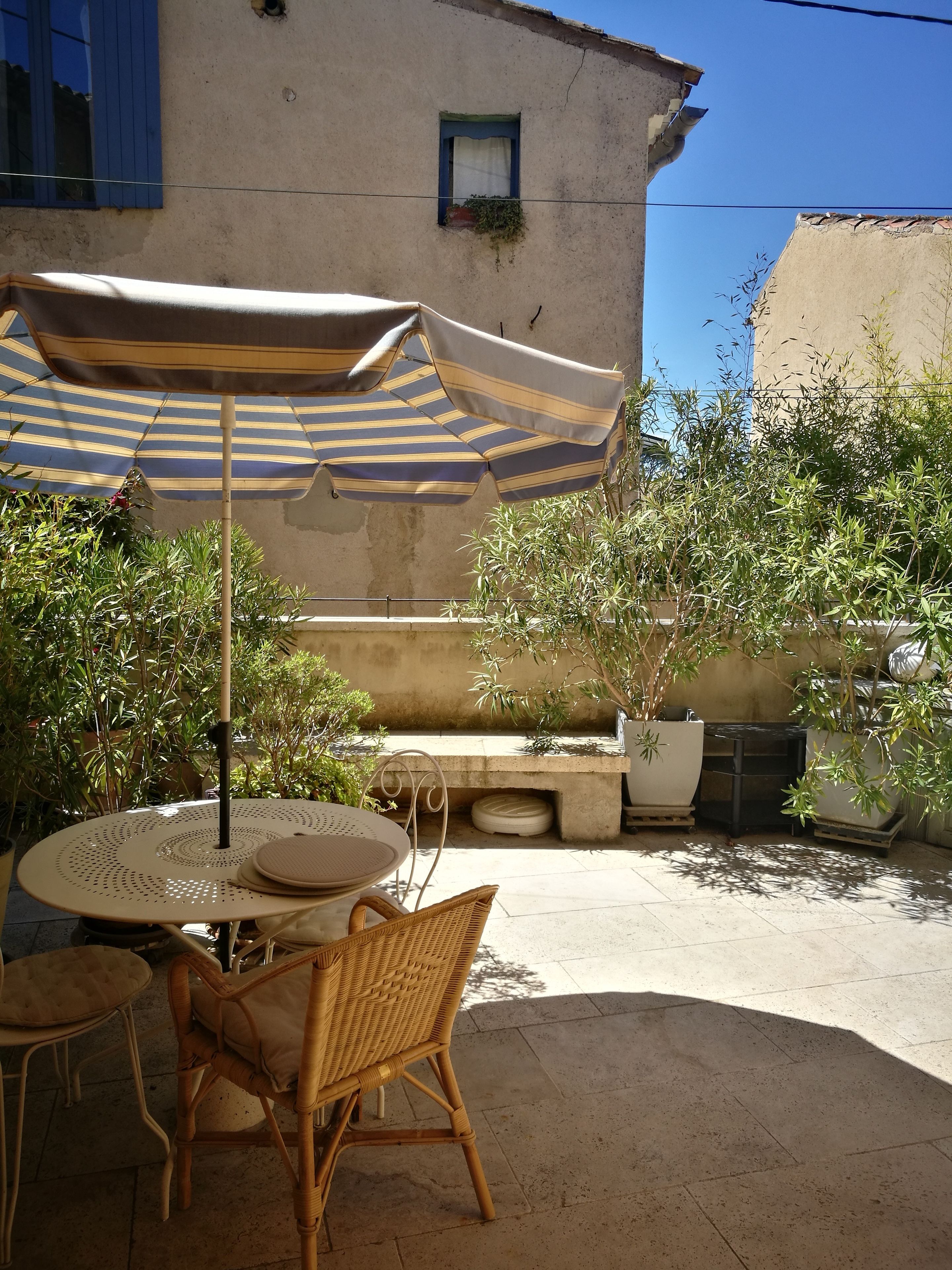 A patio with a round table and wicker chairs, a striped umbrella, and potted plants.
