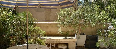 A patio with a round table and wicker chairs, a striped umbrella, and potted plants.