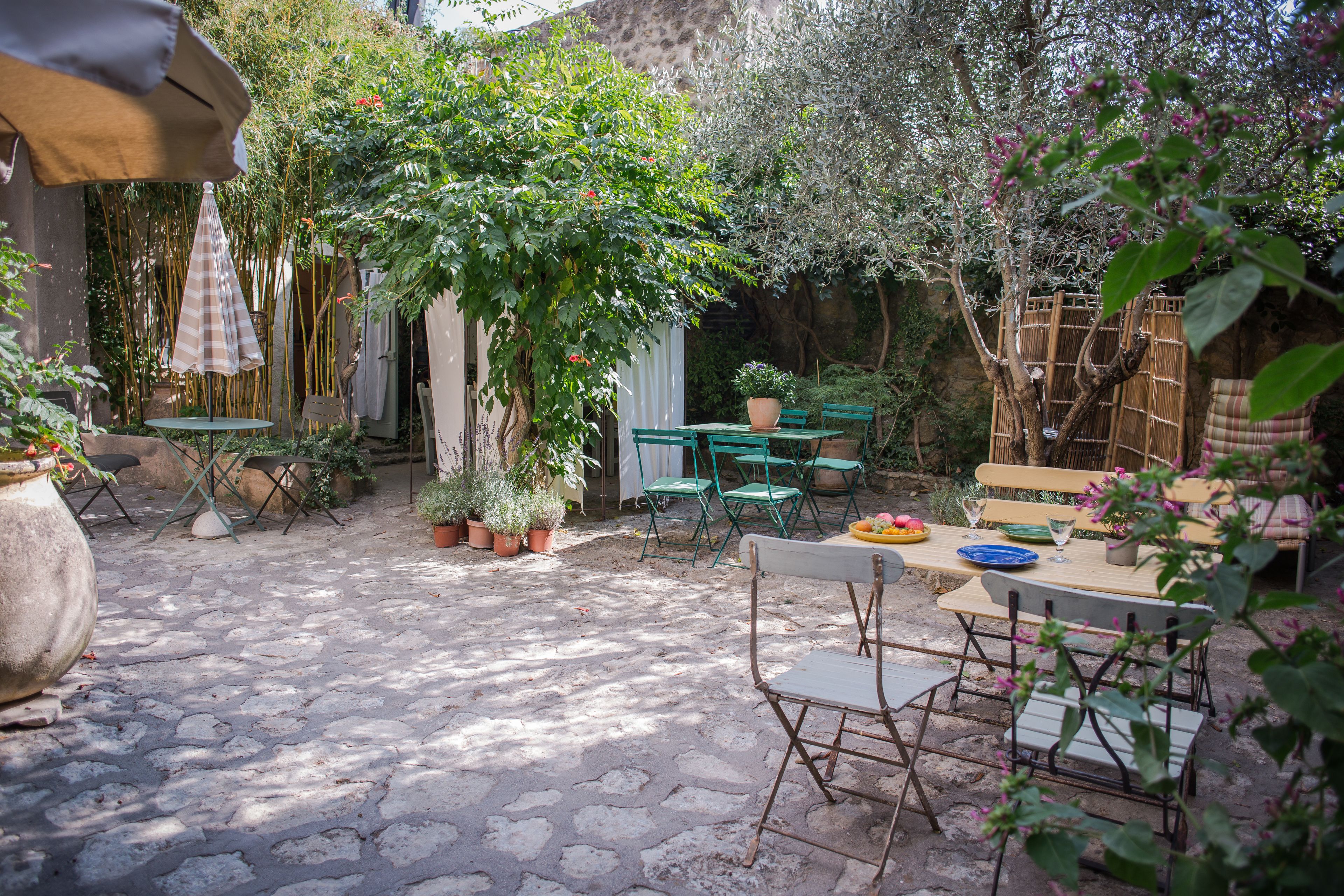 Un patio con mesa y sillas, rodeado de plantas en macetas y una valla de bambú.