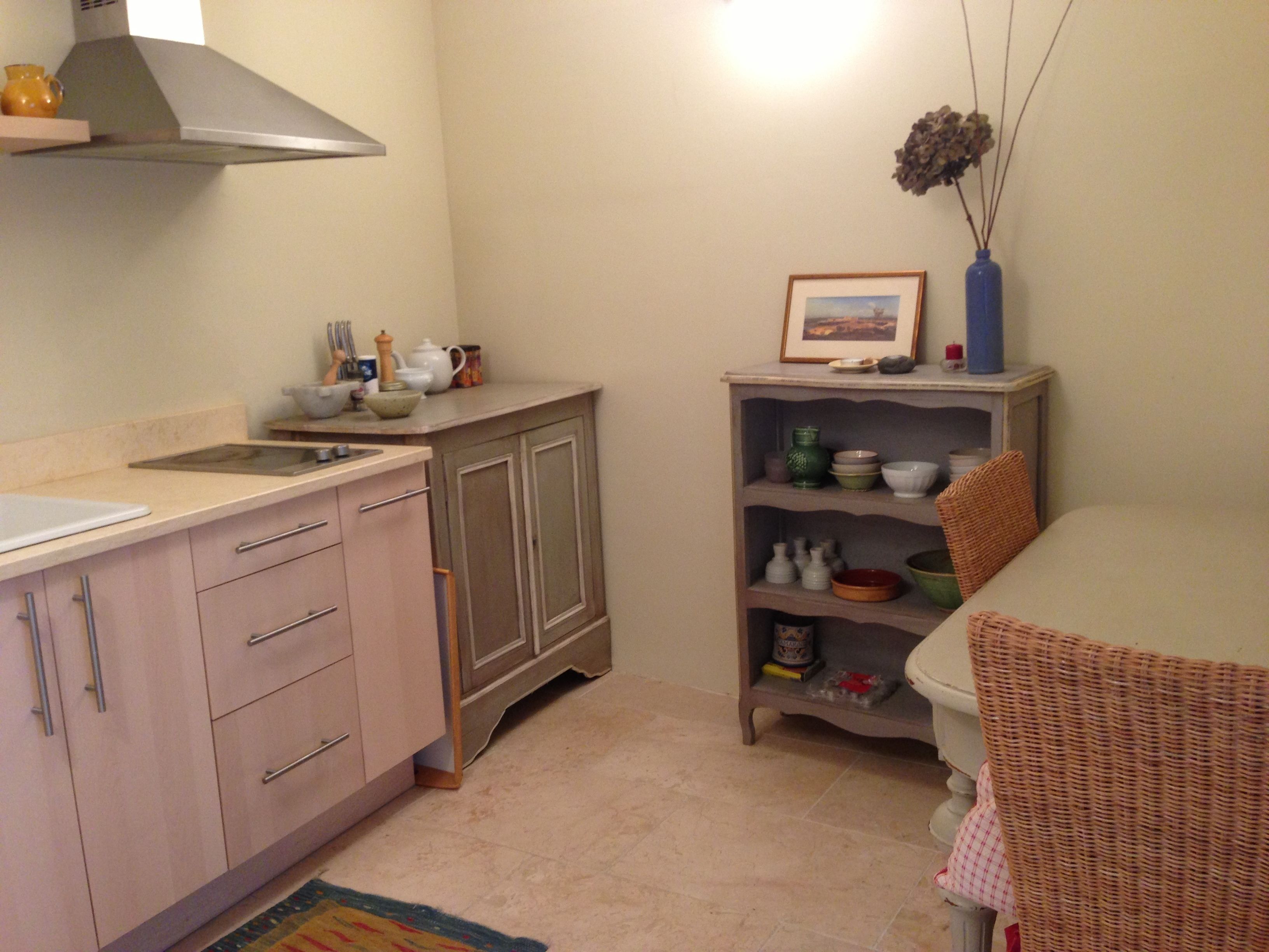 Una cocina con pileta, encimera, alacenas y un estante con varios objetos.