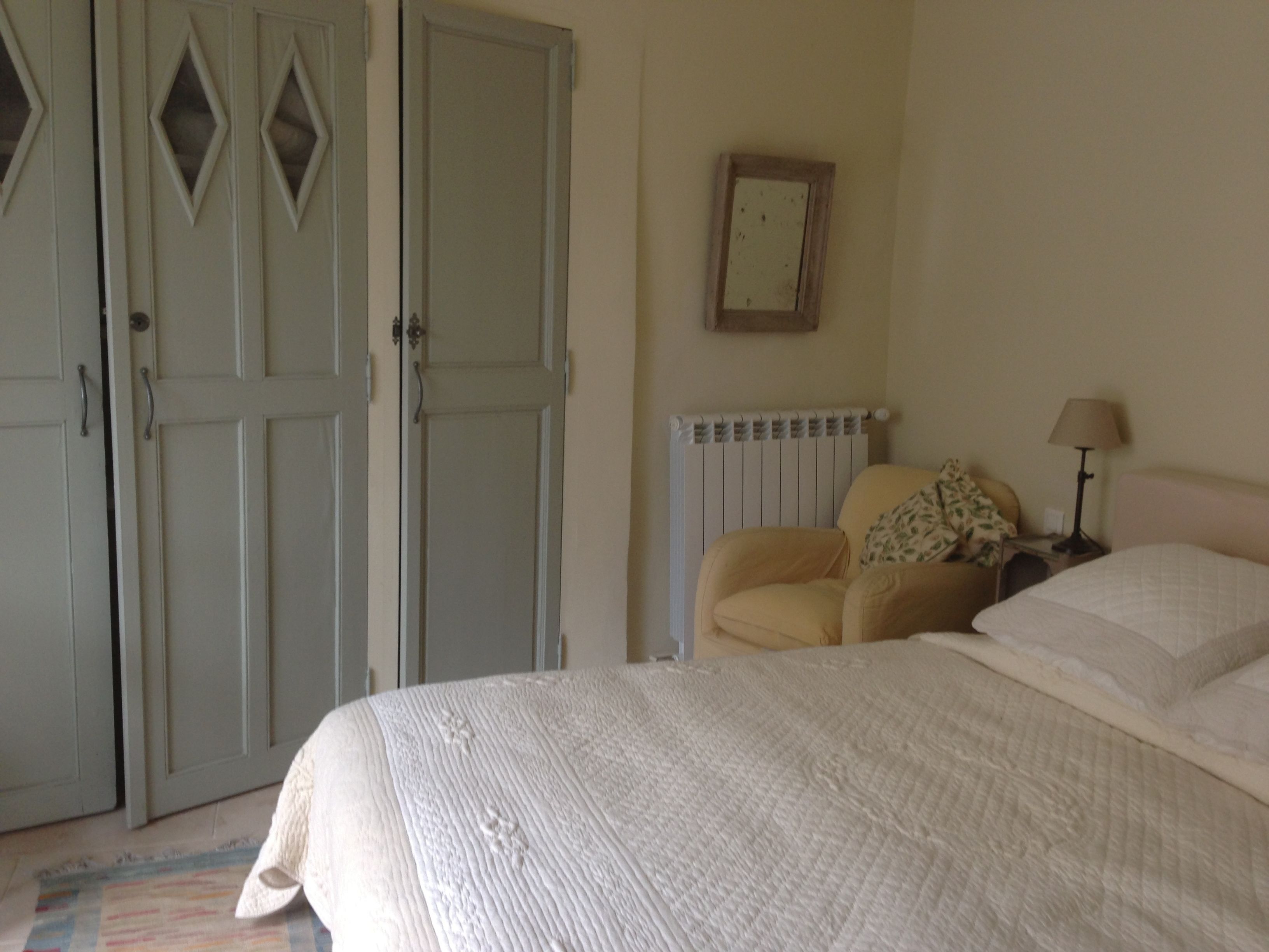 A bedroom with a bed, a chair, a radiator, and a wardrobe.